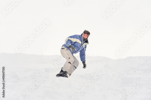 A snowboarder rushes along a snowy slope in the mountains. Freeride on a snowboard. The guy is snowboarding, snow splashes fly to the sides