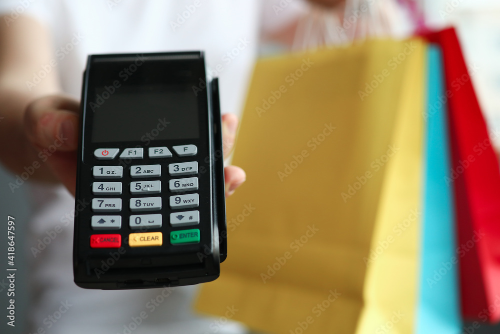 Mans hand holding pos terminal and many multicolored shopping bags closeup. Payment by credit bank card concept