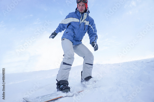 A snowboarder rushes along a snowy slope in the mountains. Freeride on a snowboard. The guy is snowboarding, snow splashes fly to the sides © Serhii Prystupa