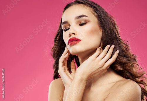 Sexy brunette with red lips on a pink background touch her hair with her hands