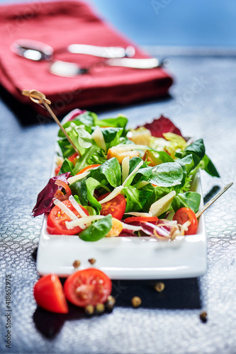 Fresh mixed salad with endive and cherry tomatoes on black plate dining, pouring olive oil