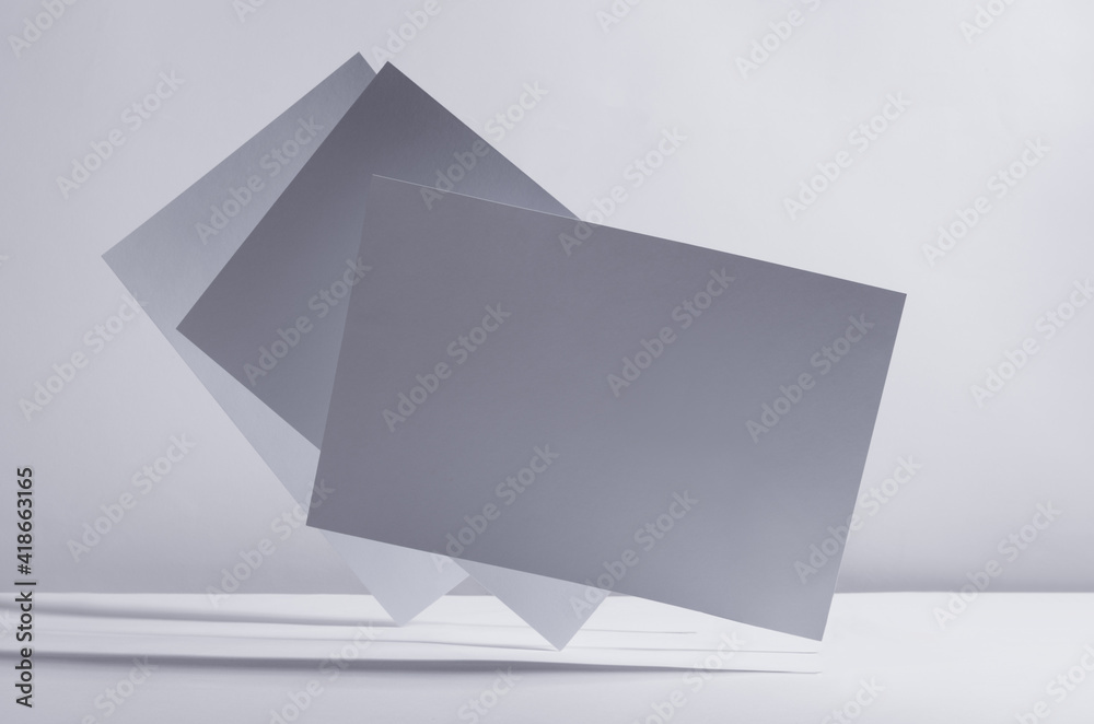 Modern simple geometric white grey abstract background with flying blank rectangle papers in light with shadow. Modern simple geometric white grey abstract background with flying blank rectangle papers in light with shadow.