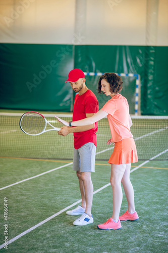 Man in a red cap and with a racket having a workout with his coach