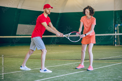 Young man in a red cap and with a racket having a workout with his female coach