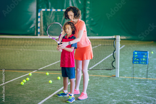 Female coach in bright clothes teaching a boy to play tennis © zinkevych