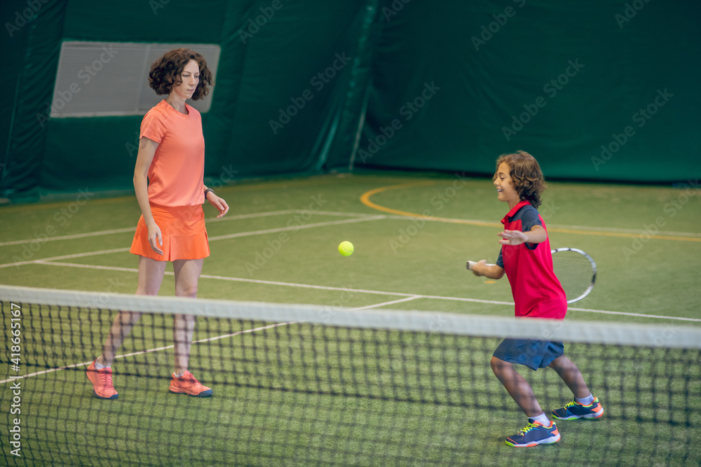 Female coach in bright clothes teaching a boy to play tennis in a gym Female coach in bright clothes teaching a boy to play tennis in a gym