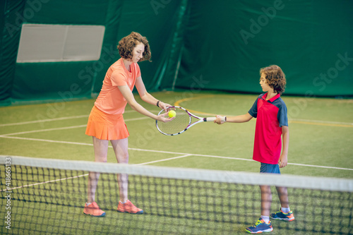 Female coach in bright clothes teaching a boy to play tennis