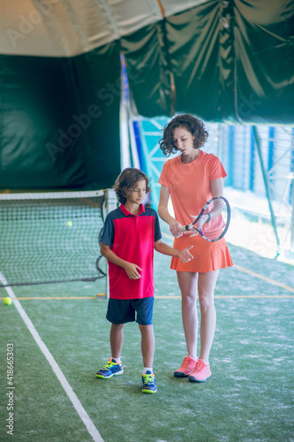 Female coach in bright clothes teaching a boy to hold a tennis racket © zinkevych