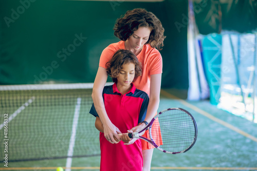 Female coach in bright clothes teaching a boy to hold a tennis racket