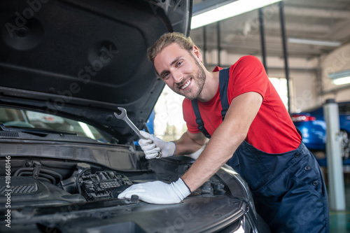 Smiling man with wrench near car hood