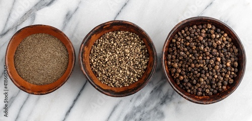 Organic dried Black Peppercorns and peppers are coarse and fine ground in a clay bowls on a marble background close-up. Seasonings and spices.  Selective Focus, banner, long picture photo