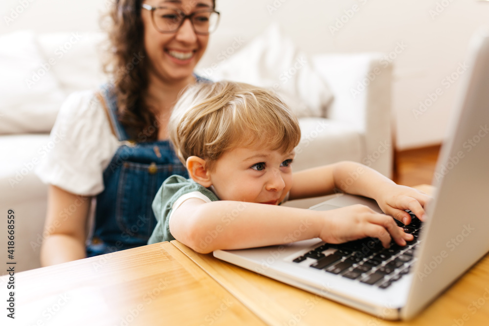 Child using laptop at home with mom smiling Child using laptop at home with mom smiling