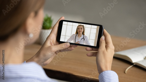 Close up view of woman talk speak on video call on smartphone with young Caucasian nurse or doctor. Female have online webcam consultation with GP or therapist on cellphone. Virtual event concept.