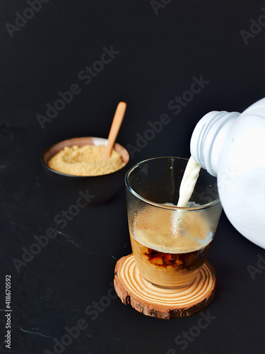 sirviendo leche en un vaso de café, y de fondo una azucarera con azúcar moreno y una cuchara de madera photo