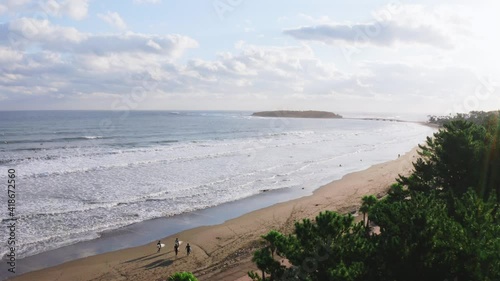Drone shot of beautiful beach in Japan with group of man walking with swimsuite and surfboard. Sun rise at Aoyama beach in Miyazaki, Japan.