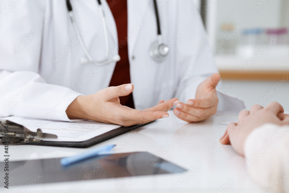 Unknown woman-doctor and patient discussing something while sitting at the table in clinic, close-up. Medicine concept Unknown woman-doctor and patient discussing something while sitting at the table in clinic, close-up. Medicine concept