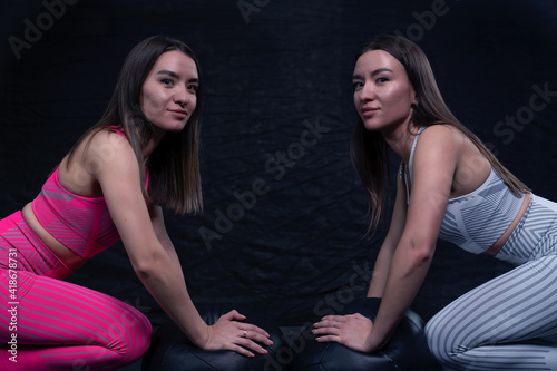 female twin sisters in sportswear designed for fitness, posing against a dark background