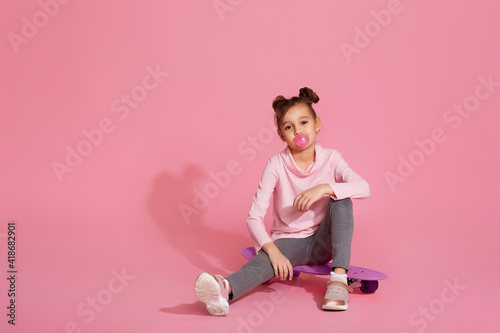 cool little child girl with chewing gum sitting on skateboard