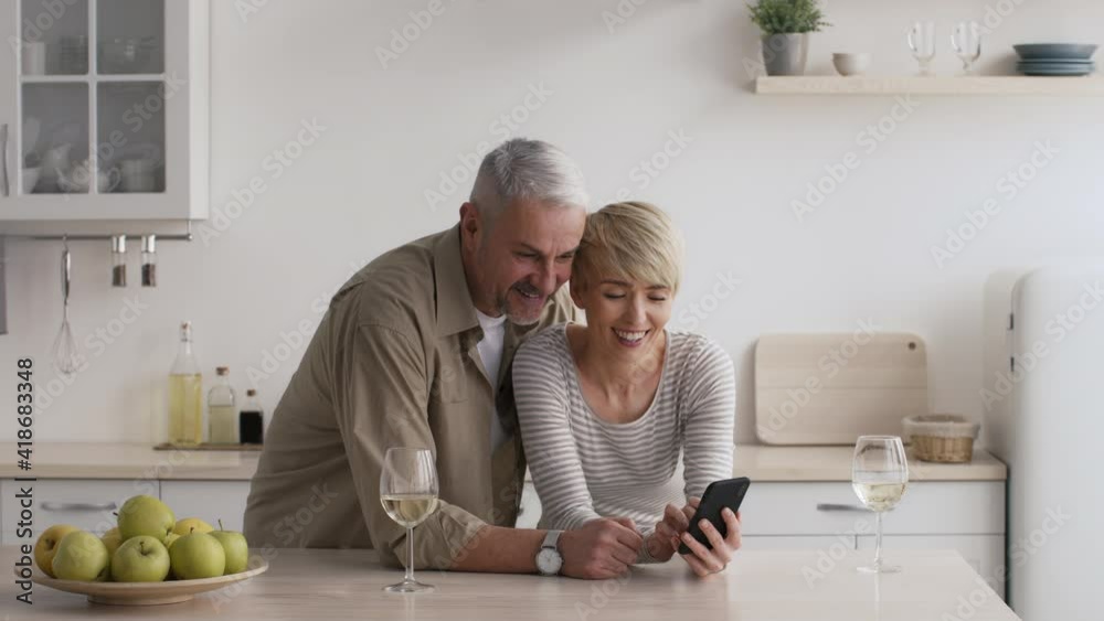 Mature Couple Using Smartphone In Modern Kitchen At Home Mature Couple Using Smartphone In Modern Kitchen At Home