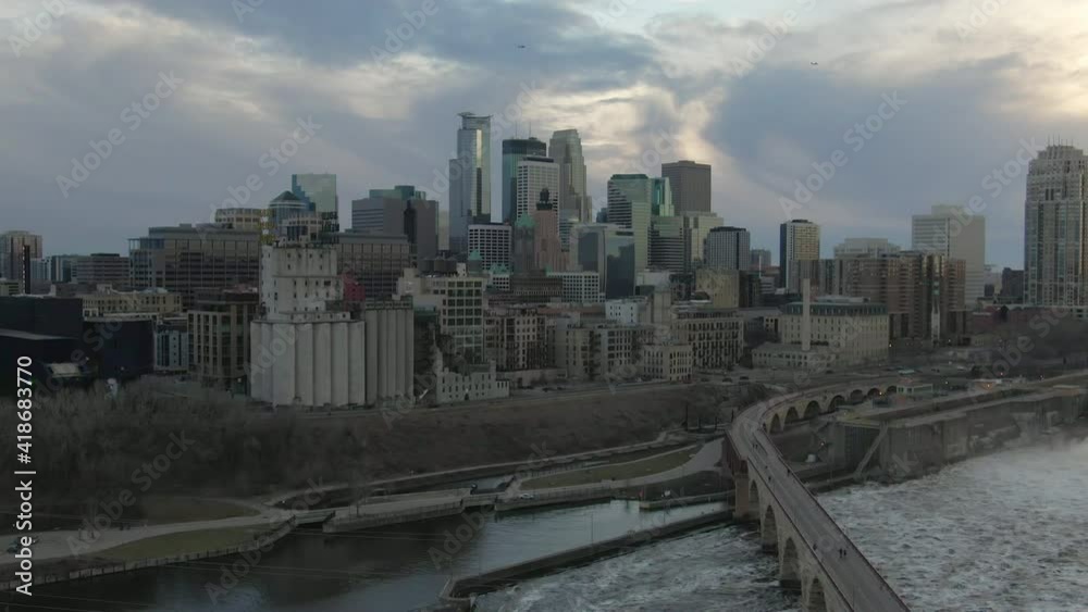Aerial shot of bridge over canal by downtown against sky, drone descending over river in city during sunset - Minneapolis, Minnesota Aerial shot of bridge over canal by downtown against sky, drone descending over river in city during sunset - Minneapolis, Minnesota