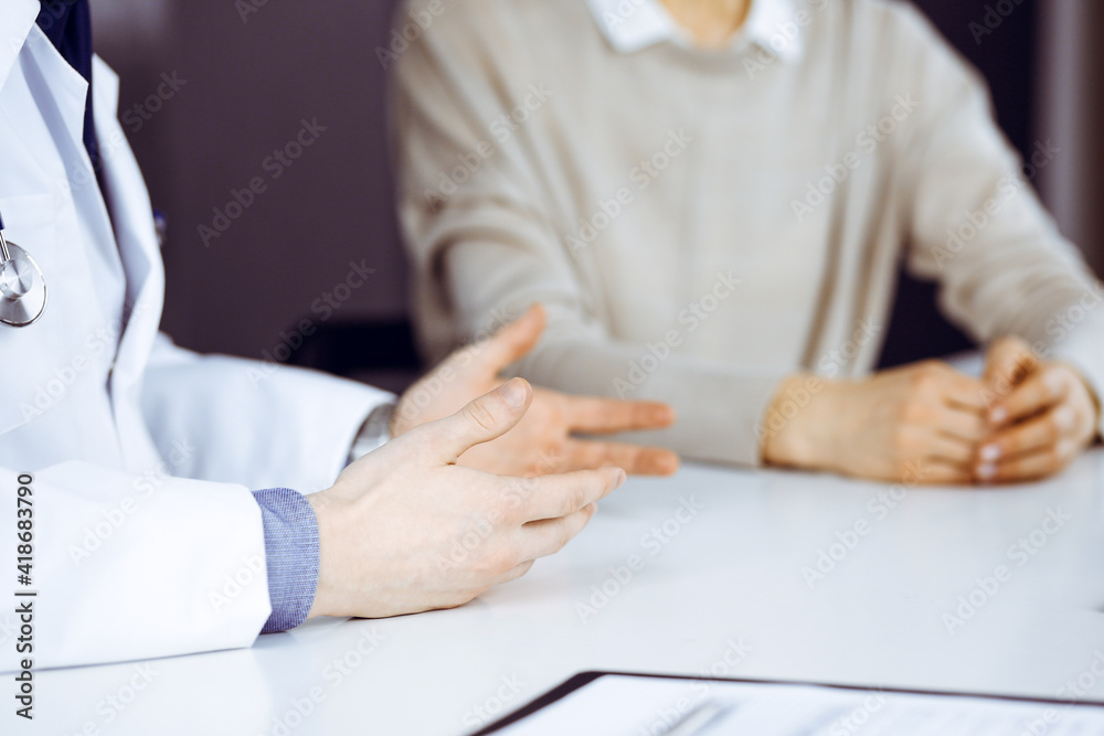 Unknown male doctor and patient woman discussing something while sitting in clinic. Best medical service in hospital, medicine, pandemic stop