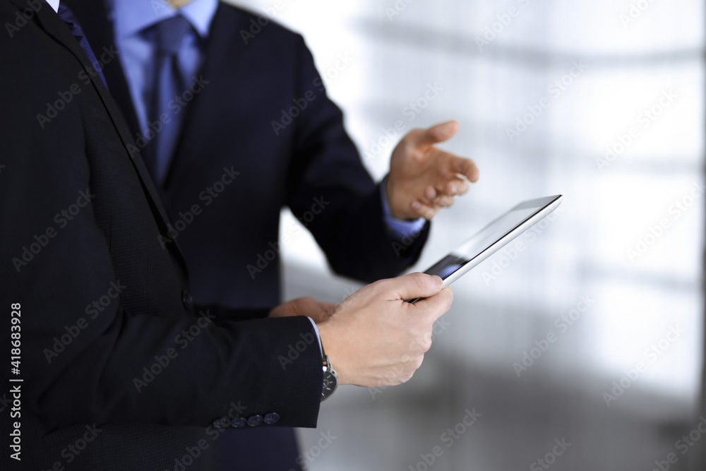 Business people use a tablet computer for discussion of their new project, standing in a modern office. Unknown businessman or male entrepreneur with a colleague at workplace. Teamwork and partnership Business people use a tablet computer for discussion of their new project, standing in a modern office. Unknown businessman or male entrepreneur with a colleague at workplace. Teamwork and partnership
