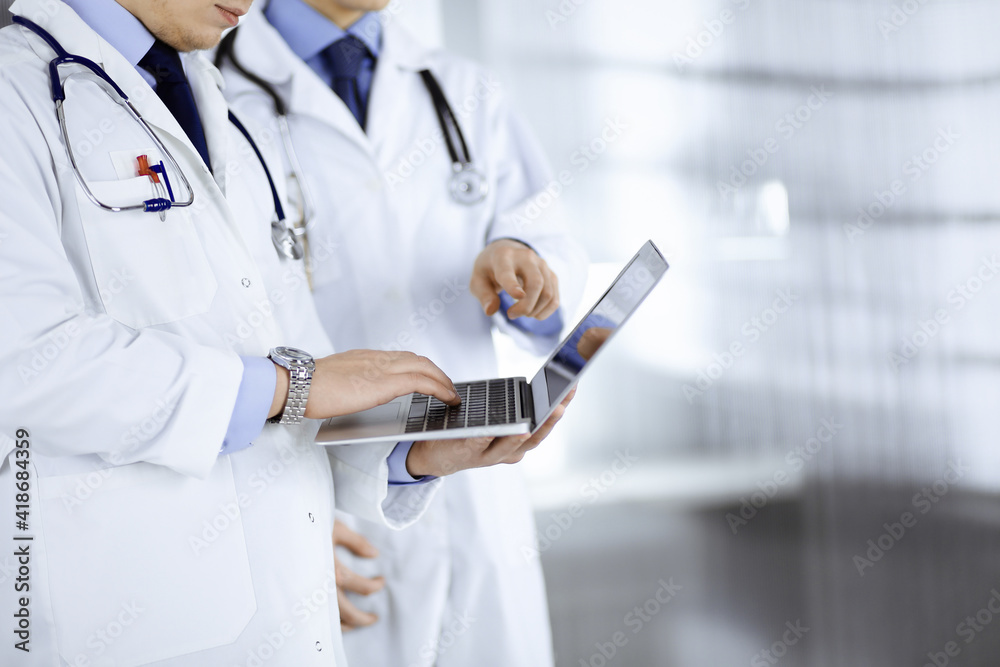 Two unknown doctors with stethoscopes discuss medical exam resoults, while standing at hospital office. Physicians using a laptop for checking up medication names records. Perfect medical service in Two unknown doctors with stethoscopes discuss medical exam resoults, while standing at hospital office. Physicians using a laptop for checking up medication names records. Perfect medical service in
