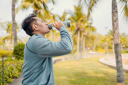 Young sport man drink water after jogging, running in the park. Sport thirsty and resting after exercise.