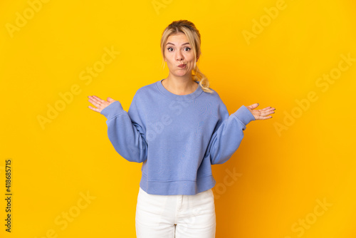 Young Russian woman isolated on yellow background having doubts while raising hands