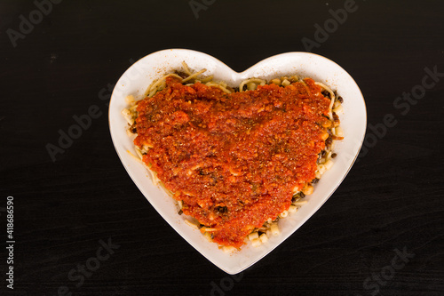 Famous traditional Arabic, Egyptian dish - Koshari. National Kushari in a white heart plate on dark wooden background. Flat lay, top view. with tomato sauce photo