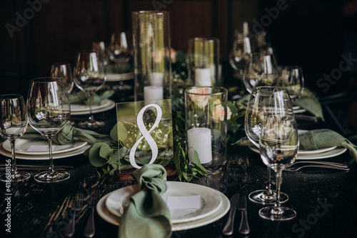 Wedding banquet. The festive table is served with plates with napkins and name cards, glasses and cutlery, and decorated with flower arrangements and candles © AlexGukalovUkraine