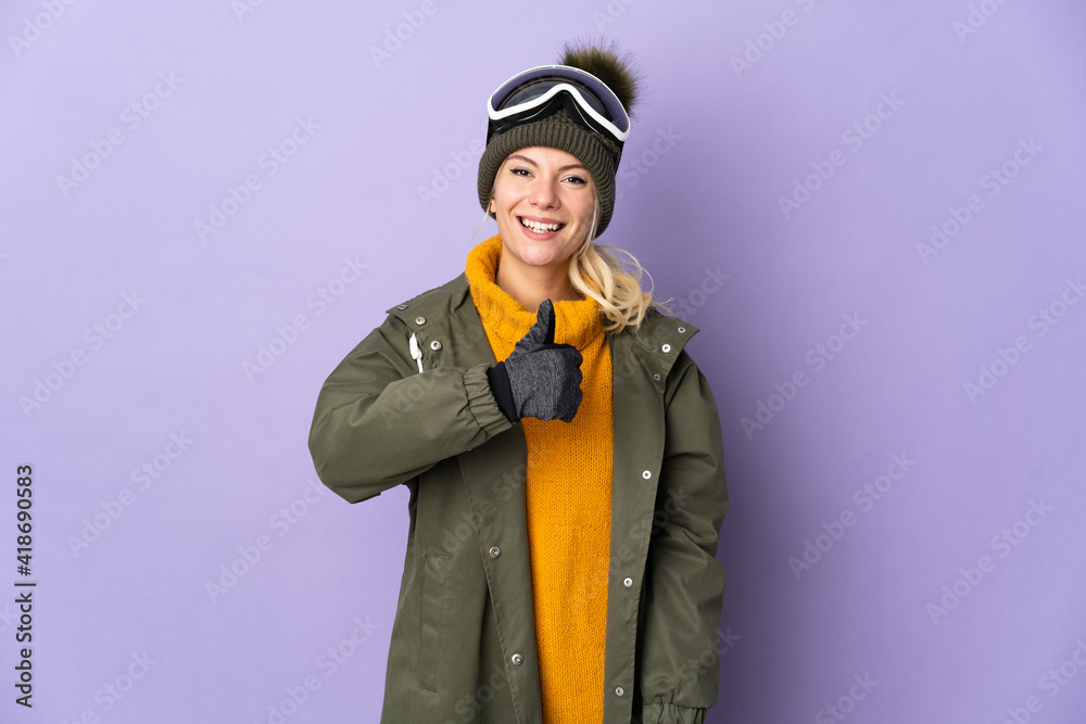 Skier Russian girl with snowboarding glasses isolated on purple background giving a thumbs up gesture
