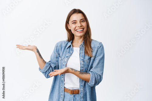 Introducing product to you. Smiling young woman demonstrating an advertisement on white copy space, presenting somethin for client, standing against white background photo