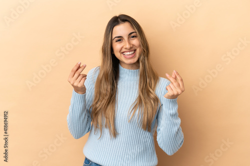 Young caucasian woman isolated on beige background making money gesture