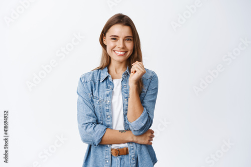 Happy successful woman standing in casual outfit, smiling pleased at camera and looking confident, standing against white background