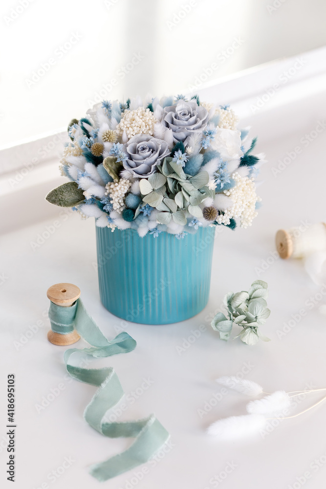 Bouquet with roses, hydrangea and spikelets in blue colors. Stabilized flowers in a blue ceramic vase at home on the dressing table. Interior decor.
