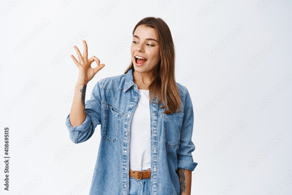 Alright. Smiling cute girl showing okay sign and say yes, approve something good, like and agree, standing pleased against white background Alright. Smiling cute girl showing okay sign and say yes, approve something good, like and agree, standing pleased against white background