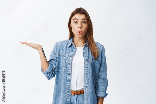 Portrait of excited blond woman showing advertisement, holding product on palm against white empty space, demonstrate something in hand, white background