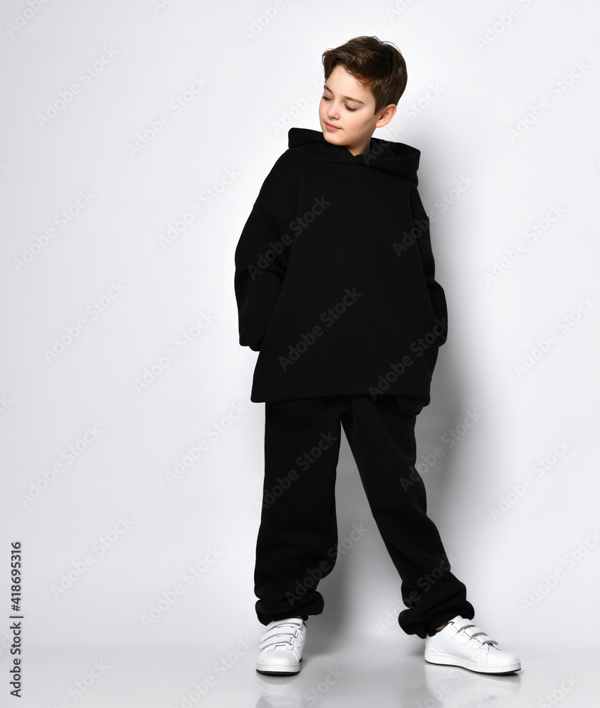 Cute stylish kid in colourful sportsuit standing with hood over head pointing fingers at camera. Fashionable sporty kids, healthy leisure, happy childhood. Full length portrait isolated on light grey Cute stylish kid in colourful sportsuit standing with hood over head pointing fingers at camera. Fashionable sporty kids, healthy leisure, happy childhood. Full length portrait isolated on light grey