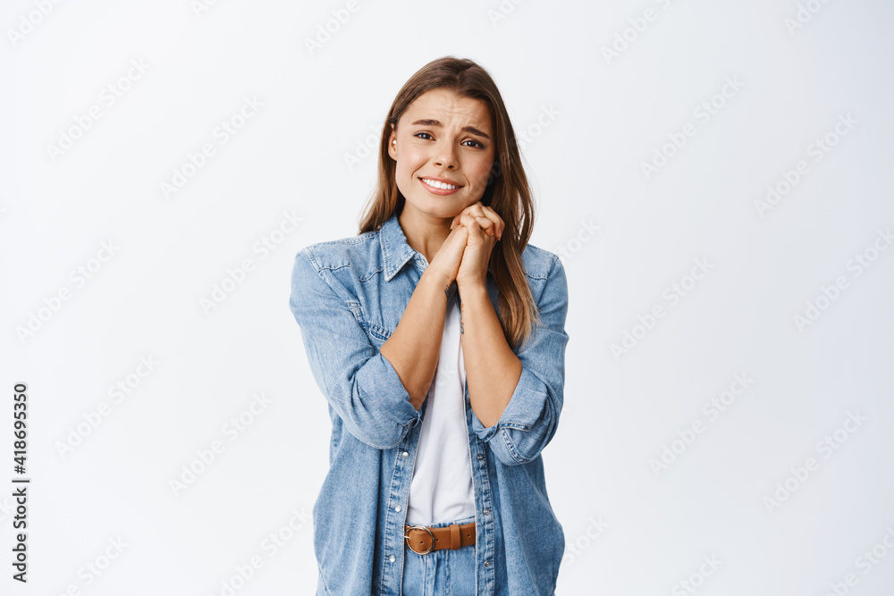 Portrait of young girl feeling touched and heartwarmed, holding hands near face and melting from something beautiful or romantic, staring fascinated at camera, white background Portrait of young girl feeling touched and heartwarmed, holding hands near face and melting from something beautiful or romantic, staring fascinated at camera, white background