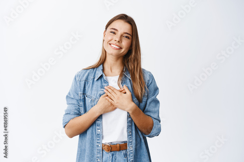 Фотография Portrait of touched young woman feeling flattered, holding hands on heart and sm