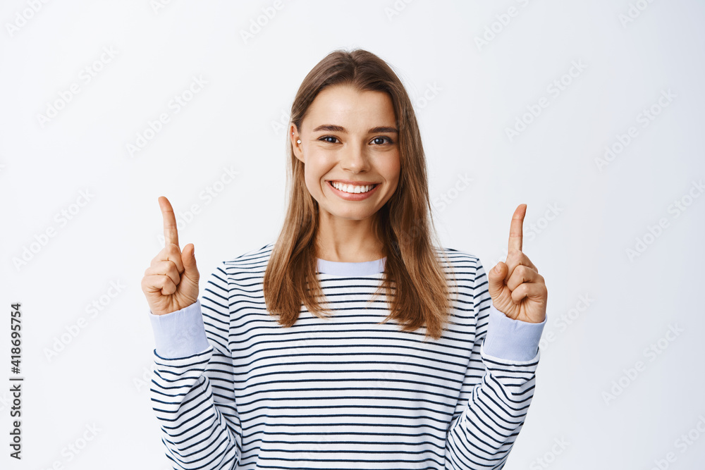 Close up portrait of smiling blond woman pointing fingers up, showing advertisement, giving recommendation, demonstrating promo offer, white background Close up portrait of smiling blond woman pointing fingers up, showing advertisement, giving recommendation, demonstrating promo offer, white background