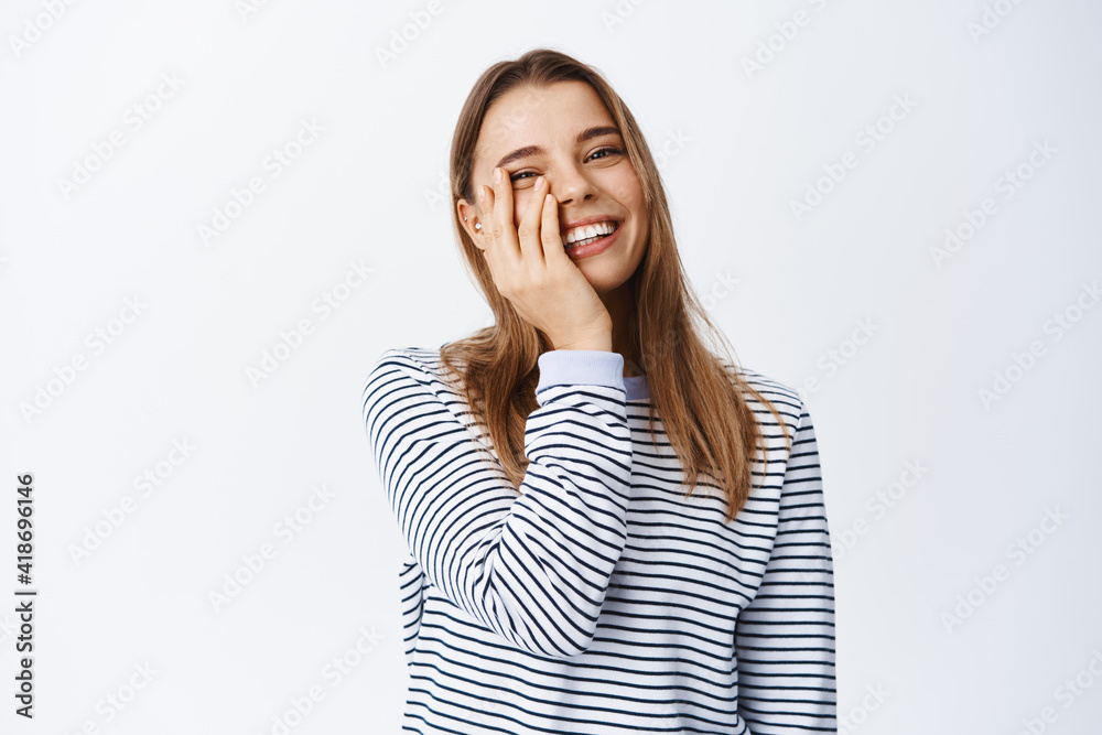 Beauty. Happy candid girl with natural light make up, touching face and smiling with white healthy teeth, standing carefree against white background Beauty. Happy candid girl with natural light make up, touching face and smiling with white healthy teeth, standing carefree against white background