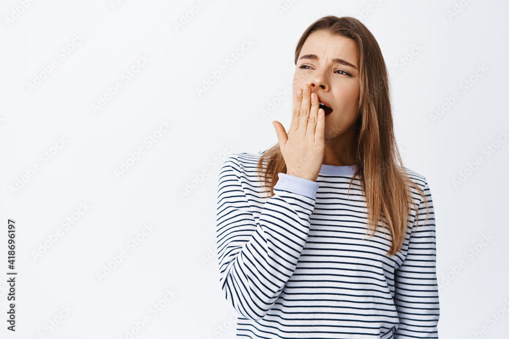 Portrait of young woman feeling tired, yawning and covering opened mouth with hand, standing sleepy or bored, standing over white background Portrait of young woman feeling tired, yawning and covering opened mouth with hand, standing sleepy or bored, standing over white background