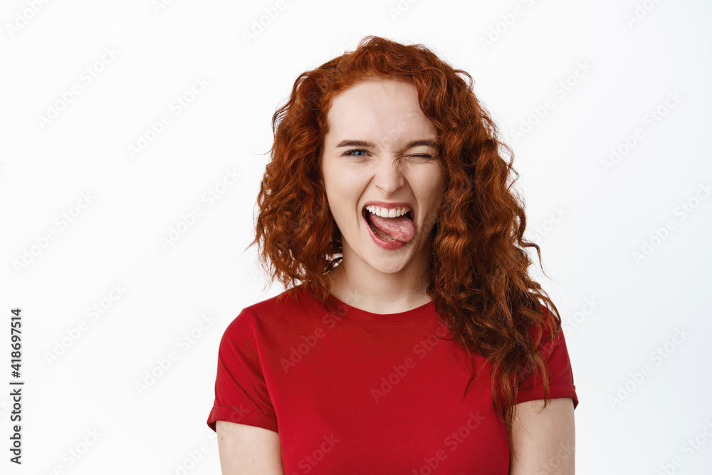 Portrait of carefree young teen ginger girl making positive funny faces, showing tongue and smiling, winking at camera to motivate and encourage you, white background Portrait of carefree young teen ginger girl making positive funny faces, showing tongue and smiling, winking at camera to motivate and encourage you, white background