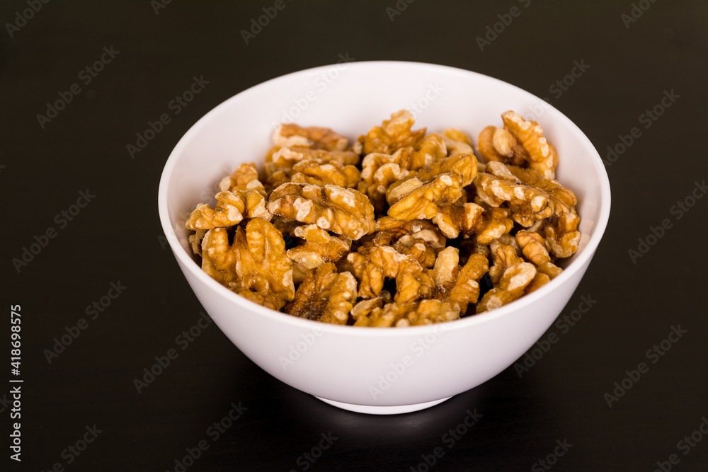 Walnuts, a bunch of peeled walnuts in white bowl on black table Walnuts, a bunch of peeled walnuts in white bowl on black table