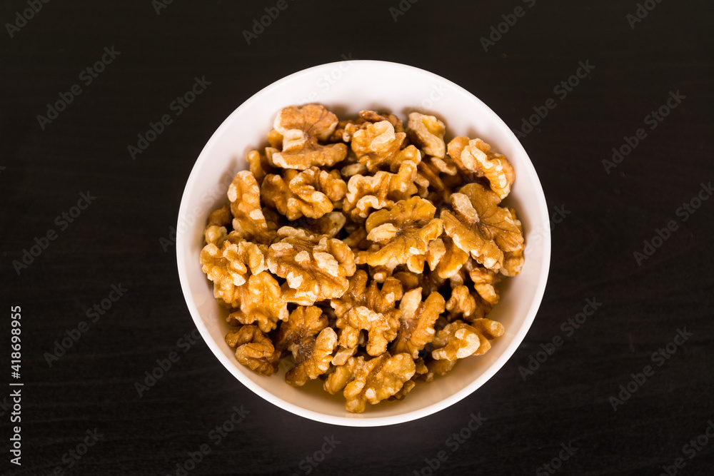 Walnuts, a bunch of peeled walnuts in white bowl on black table top view Walnuts, a bunch of peeled walnuts in white bowl on black table top view