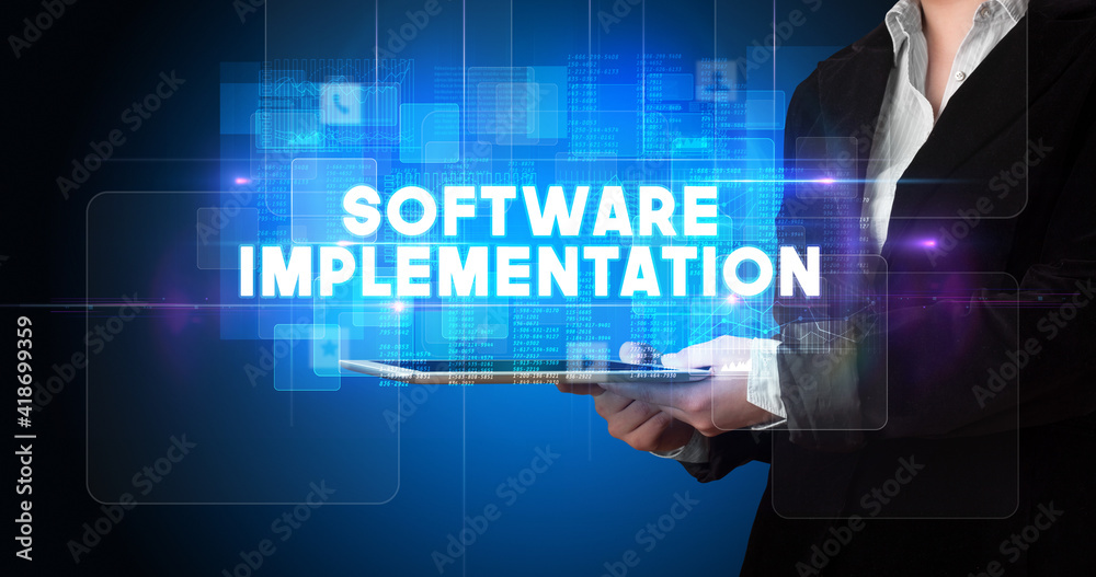Young business person working on tablet and shows the inscription: SOFTWARE IMPLEMENTATION Young business person working on tablet and shows the inscription: SOFTWARE IMPLEMENTATION
