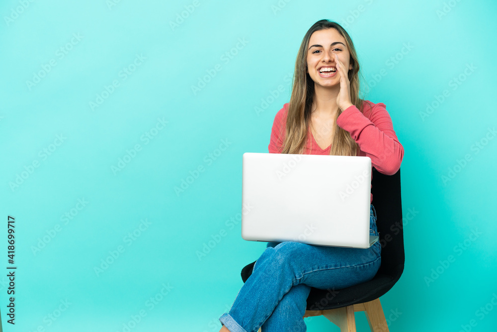 Young caucasian woman sitting on a chair with her pc isolated on blue background shouting with mouth wide open Young caucasian woman sitting on a chair with her pc isolated on blue background shouting with mouth wide open