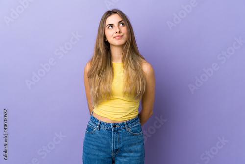 Young woman over isolated purple background and looking up © luismolinero